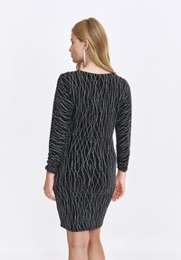 Czarna sukienka typu bodycon z długimi rękawami, z teksturowanym srebrnym wzorem fal. Tkanina ma błyszczące wykończenie, podkreślające sylwetkę.