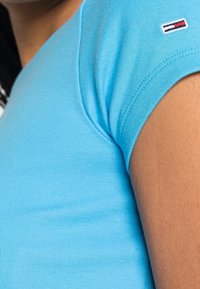 Vaaleansininen ribattu lyhythihainen t-paita, jossa on sopiva muotoilu ja pieni merkkilogo-patch, jossa on punaista ja tummansinistä raitaa olkapäillä.