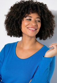 Blaues Langarmshirt mit Rundhalsausschnitt, getragen von einer Person mit lockigem Haar. Der Stoff scheint weich mit einer glatten Textur zu sein.