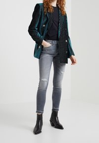 Svart sammet blazer med turkosa ränder, dubbelknäppt design, i kombination med grå, rivna, skinny jeans och svarta ankelboots.