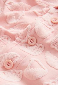 Tissu rose doux avec des motifs en relief en forme de panier et des boutons roses assortis le long d’une couture.