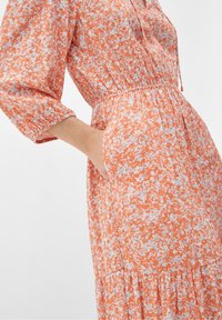 Pomarańczowa sukienka w kwiatowy wzór z rękawami do trzech czterech, elastycznym pasem i kieszeniami. Wykonana z lekkiego materiału z warstwowym dołem.