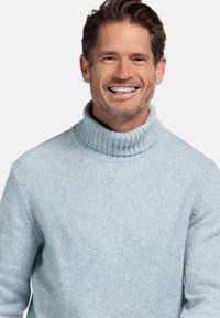 Lichtblauwe coltrui, met ribbelkraag, zachte structuur en gebreid patroon, gedragen door een glimlachende man tegen een effen achtergrond.