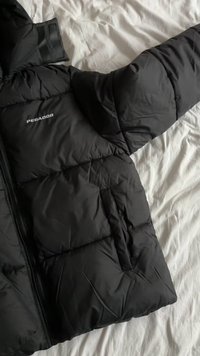 Svart dunjakke med glidelås, med hette og elastiske mansjetter. Inkluderer en vertikal glidelåslomme og en logo på brystet.