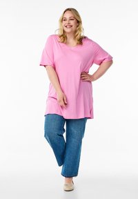 Loose pink V-neck top with short sleeves, paired with wide-leg blue jeans. The fabric appears soft with a smooth texture.