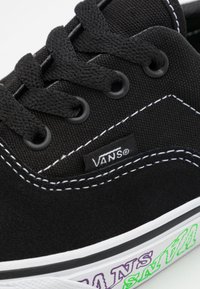 Baskets en toile noire avec une finition en suède, dotées de lacets noirs, de coutures blanches et d'un logo coloré imprimé sur la semelle.