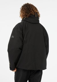 Juodas paminkštintas švarkas su gobtuvu, logotipu ant kairiojo rankovės ir laisvu siluetu. Lygus, tekstūruotas audinys.