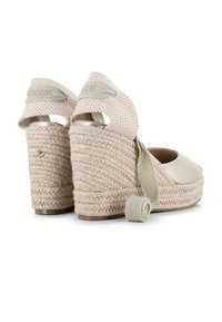 Sandalias de cuña de esparto beige con tacón de yute, superficie tipo satén y correas de tejido texturizado. Presenta un detalle de cinta enrollada en el costado.
