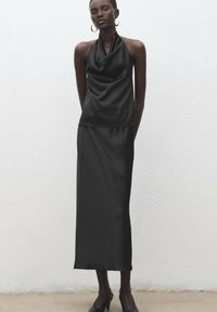 Čierny saténový halternový top s drapovaným výstrihom kombinovaný s dlhou sukňou, ktorá má hladký pocit a jednoduchý siluetu.