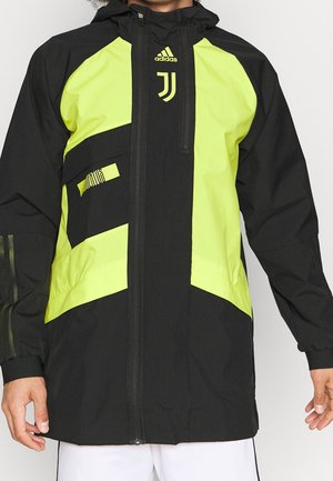 Czarna i jasnofioletowa kurtka sportowa Adidas Juventus z pełnym zamkiem błyskawicznym i logo na piersi, noszona przez osobę widoczną od szyi do bioder.