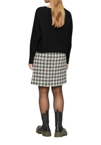 Schwarzer gerippter Pullover, Hahnentritt-Rock in Schwarz und Weiß und schwarze Lederstiefeletten mit grünen Sohlen.