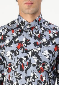 Knappskjorte i lyseblå stoff med blomsterprint i rødt, svart og hvitt; med krage og to frontknapper.