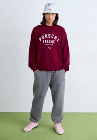 Bordeaux oversized sweatshirt med hvid "Porsche League Turbo Club" tekst, parret med grå sweatpants og lyserøde sneakers. Bucket hat med blomstermønster.