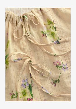 Top in tessuto beige con stampa floreale in viola e verde. Presenta un collo arricciato con lacci e sottili righe testurizzate. Leggero e morbido.