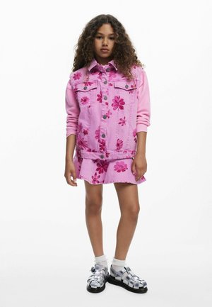 Jachetă de denim roz cu modele florale, asortată cu o rochie de denim roz. Sandale argintii cu suprafață texturată și șosete până la gleznă.