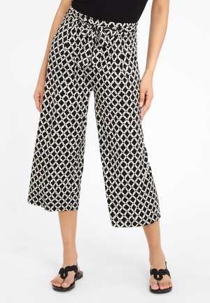 Woman wearing black and white geometric patterned wide-leg cropped pants with a tied waistband and black sandals.