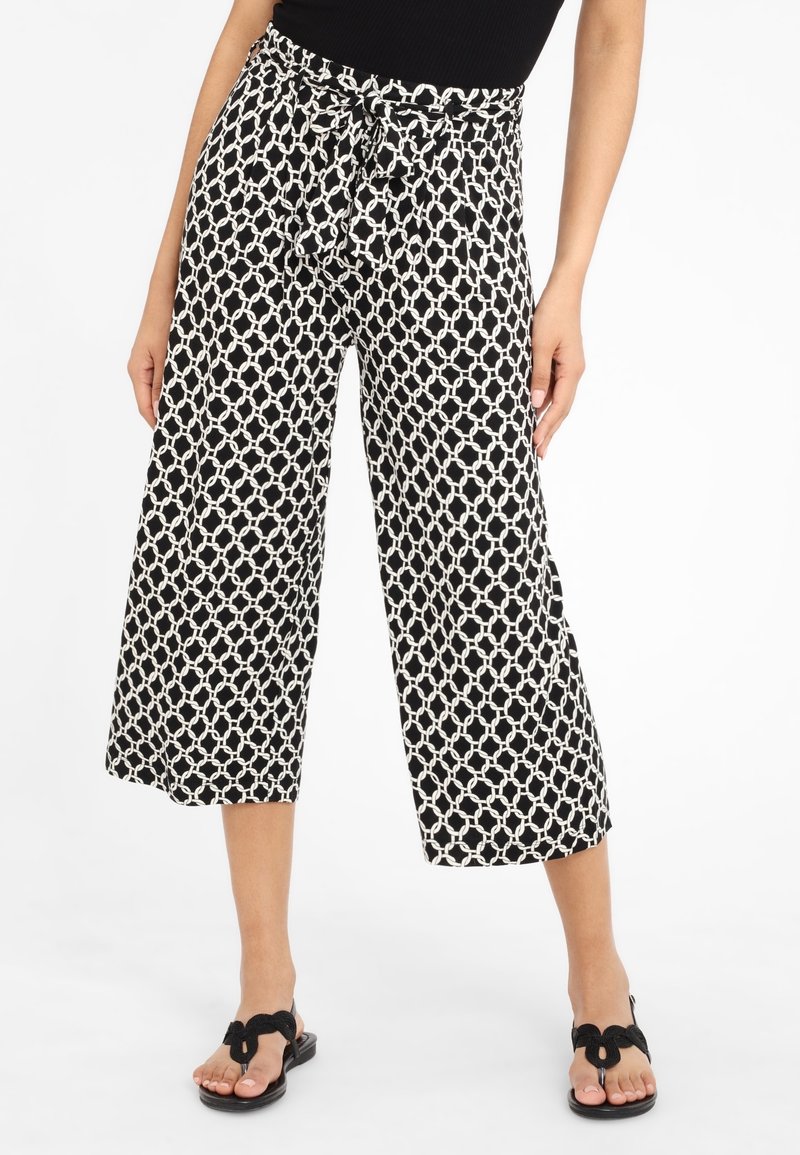 Femme portant un pantalon large court à motifs géométriques noirs et blancs avec une taille nouée et des sandales noires.