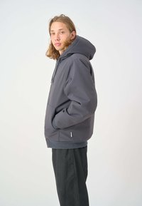 Graue Kapuzenjacke mit einer Fronttasche, elastischen Bündchen und Saum. Der Stoff wirkt glatt und hat ein minimalistisches Design ohne Verzierungen.