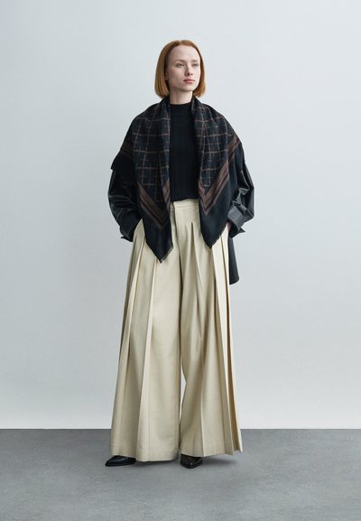 Fekete mintás sál, bordázott fekete pulóver, széles, redőzött krémszínű nadrág, fekete hegyes cipő. Egyszerű, modern kialakítás és anyagok.