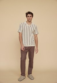 Strikket kortermet skjorte i kremfarge med brune vertikale striper, sammen med brune bukser og lysegrå slip-on sko. Minimalistisk design.