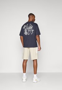 Marine bomull t-skjorte med stort hvitt New York-logo og blomsterdesign på baksiden; parret med beige shorts og hvite sneakers.