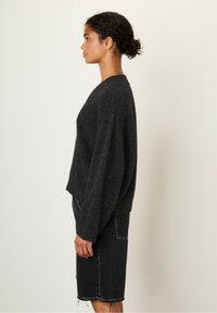 Dark gray wool sweater with a relaxed fit, wide sleeves, and ribbed cuffs, paired with a black denim skirt with distressed hem.