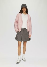 Rosa gestrickte Strickjacke, weißes T-Shirt, grauer karierten Rock, silberne Schuhe und eine graue Mütze. Kurzärmlig, Knopfverschluss an der Strickjacke.