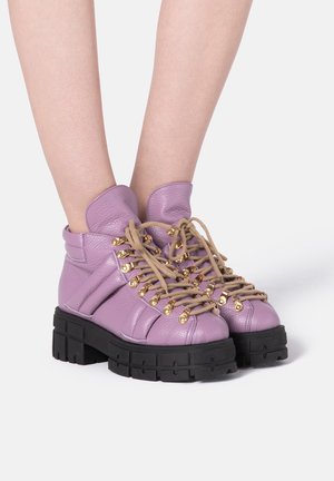 Paarse leren enkelboots met gouden oogjes, een dikke zwarte zool en beige veters. Voorzien van een gestructureerd ontwerp en een gepolsterde kraag.