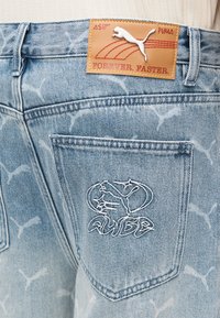 Spijkerbroek in lichtblauw met een vervaagd patroon, voorzien van een leren label met "PUMA" en een wit geborduurd logo op het achterzakje.