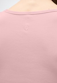 Πίσω όψη ενός ατόμου που φοράει ένα ανοιχτό ροζ ριμπ μπλουζάκι με ένα μικρό ραμμένο κύκλο στο επάνω κεντρικό μέρος της πλάτης.