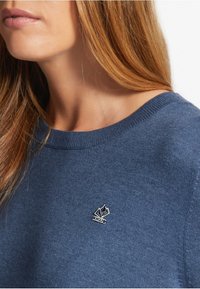 Blauer Rundhalsausschnitt-Pullover aus strukturiertem Stoff mit einem kleinen Logo, das auf der Brust gestickt ist. Klassisches Design, minimale Details.