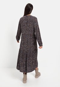 Langes, blümchenmuster Kleid in dunklen Farben mit langen Ärmeln und einem fließenden Rock, getragen zu hellbraunen Knöchelstiefeln.