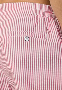 Rot-weiße gestreifte Shorts mit einem elastischen Bund und einer Rückentasche, die ein rundes Logo zeigt. Baumwollstoff mit sichtbarer Textur.