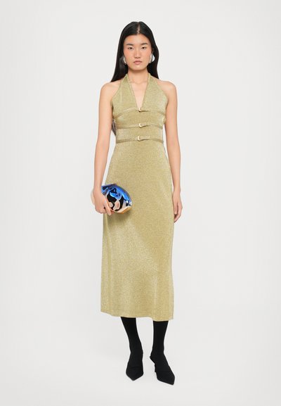 Gold halter neck dress with a fitted waist and three metallic accents; paired with a blue metallic clutch and black tights with pointed shoes.