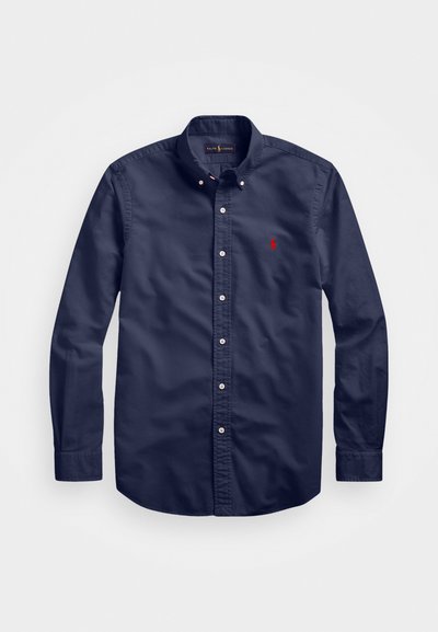 Navy blue button-down shirt with long sleeves, white buttons, and a small red logo on the left chest. Made of a smooth fabric.
