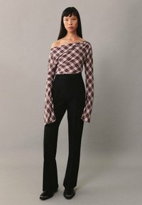 Schulterfreies Oberteil mit rot-weißem Karomuster; fließende Ärmel. Kombiniert mit hoch taillierten schwarzen Hosen. Glatte Stofftextur.