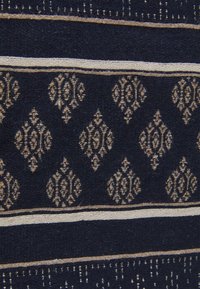 Tissu bleu marine foncé avec des motifs de diamants beiges complexes, accompagné de rayures horizontales et d'une texture tissée. Éléments décoratifs et détaillés.