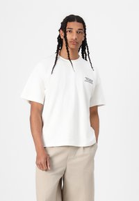 Witte katoenen t-shirt met korte mouwen en een ronde halslijn, voorzien van een kleine zwarte bedrukte graphic op de linkerkant van de borst.