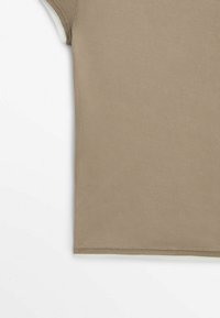 Gros plan sur la partie inférieure d'une chemise en coton côtelé beige à manches courtes sur fond blanc.