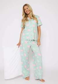 Mintgroene pyjama set met een kortemouwen overhemd met knopen en losse pasvorm broek met roze theekopjespatronen en witte tekst. Zachte stof.