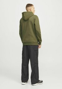 Groene hoodie met een capuchon, geribbelde manchetten en zoom, gecombineerd met losse zwarte cargobroek met zijzakken, gedragen met zwarte sneakers.