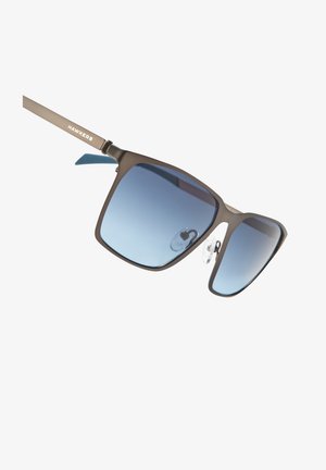 Sončna očala z mat okvirjem iz rjavega kovinskega materiala, kvadratnimi lečami, ki prehajajo od temno modre do svetlo modre, in nastavljivimi nosnimi blazinicami. Na ročaju je logotip "HAWKERS".