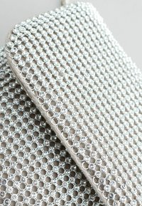 Látka zdobená rhinestones s mriežkovým vzorom. Strieborné kruhové kamene sú tesne usporiadané na béžovom pozadí, čo vytvára textúrovaný vzhľad.