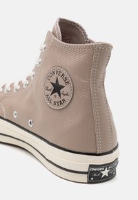 Beżowe trampki Converse Chuck Taylor All Star w wersji wysokiej, wykonane z teksturowanej skóry, z białymi oczkami, czarną gumową podeszwą i charakterystyczną łatką z logo gwiazdy.