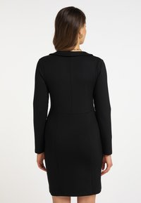Musta, vartalonmyötäinen mekko pitkillä hihoilla, pyöreällä kauluksella ja sileällä pinnalla. Ominaisuuksiin kuuluu jämäkkä siluetti ja vähäiset ompelusaumat.