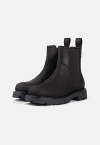 Las botas Chelsea de cuero negro presentan un acabado liso, paneles laterales elásticos, lengüetas y una suela de goma texturizada para un mejor agarre.