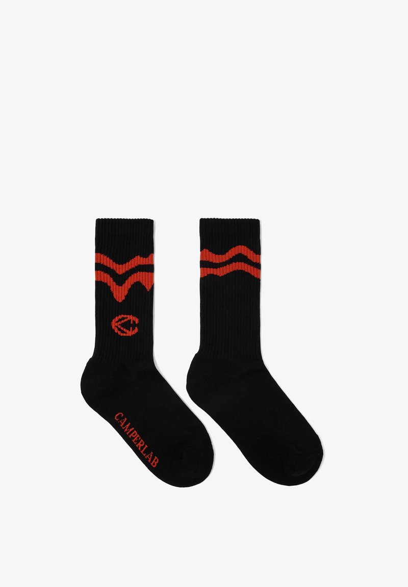 Chaussettes noires montantes avec deux rayures rouges ondulées près du haut, un logo circulaire rouge sur une chaussette, et le texte "CAMPERLAB" sur la semelle.