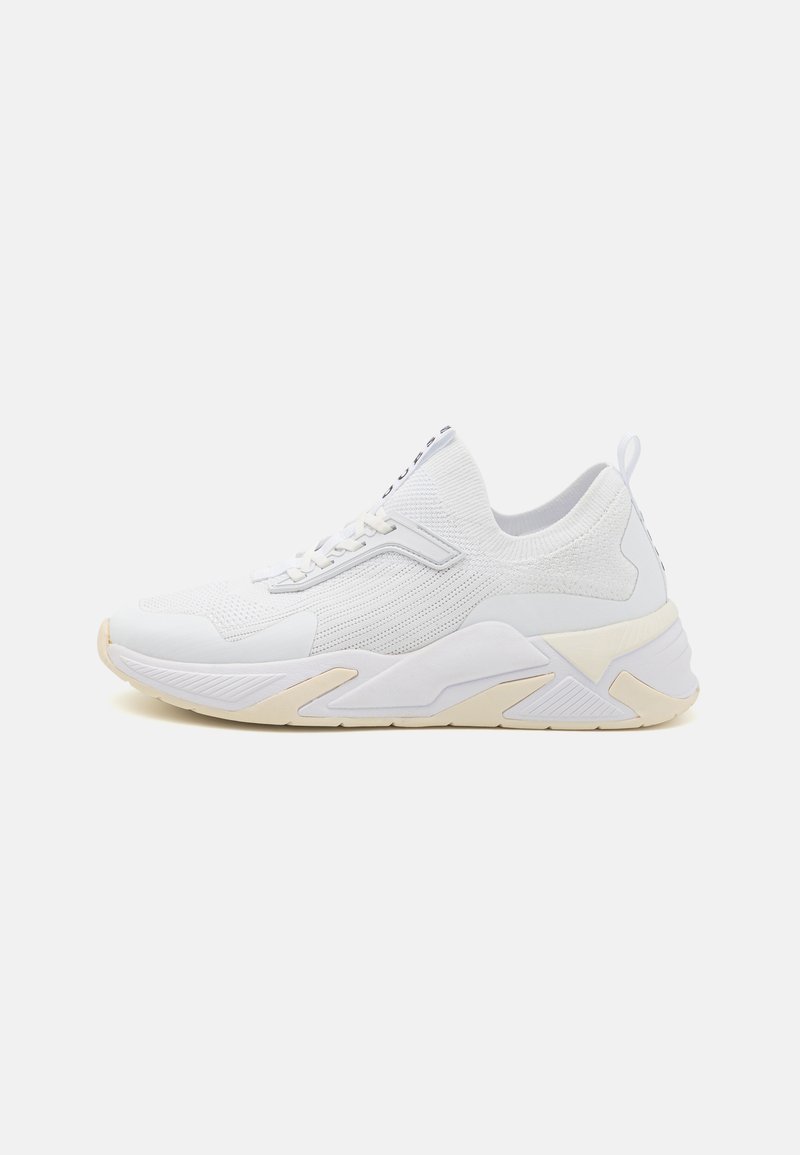 White athletic sneaker with a textured knit upper, rounded toe, and a chunky sole. Features a small loop at the heel and subtle design accents.