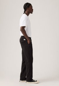 Zwarte rechte broek met een gladde textuur en subtiele zakdetails, gecombineerd met een effen witte kortemouwen shirt en zwarte sneakers.