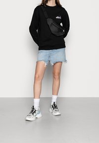 Sudadera negra con el logo "elle", minifalda de mezclilla azul con dobladillo deshilachado, calcetines blancos y zapatillas chunky multicolores. Bolso bandolera negro.